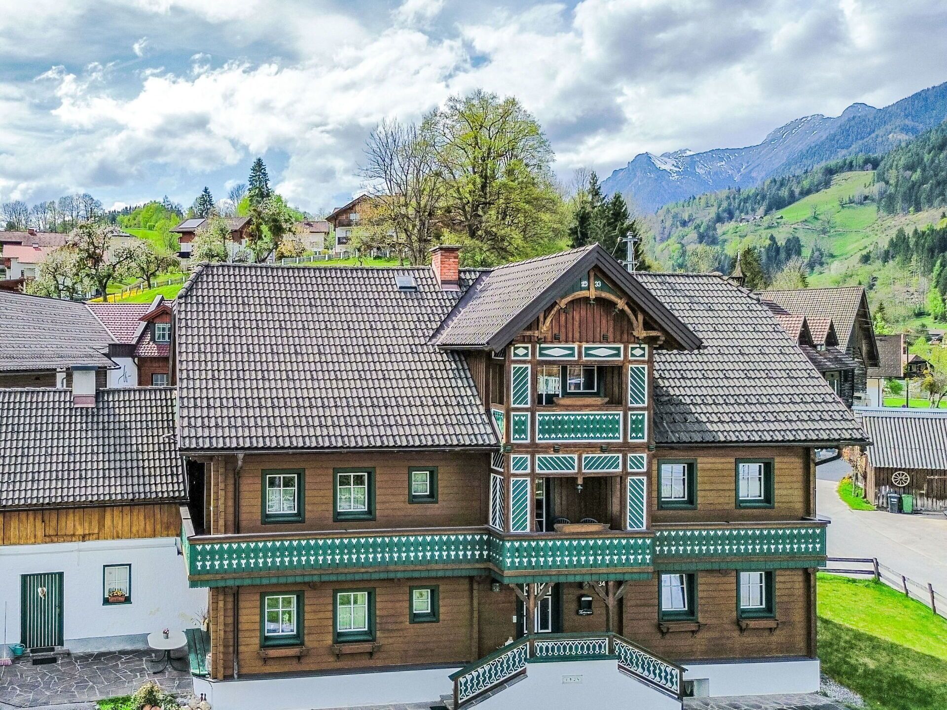 Ein traditionelles Chalet mit einem steilen Walmdach, einem Holzbalkon mit grüner Verzierung und einer Steintreppe, die zum Eingang führt.