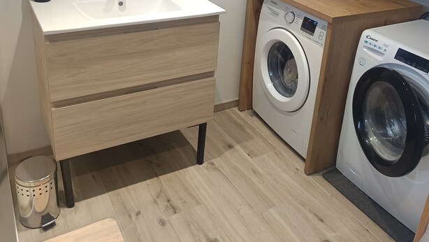 A compact kitchen with a wooden cabinet, a washing machine, and a sink with a mirror above it. - Apartment with exterior (Mirebeau)
