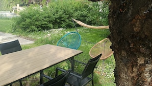 An outdoor seating area with a wooden table and black chairs, surrounded by greenery and a hammock. - Apartment with exterior (Mirebeau)