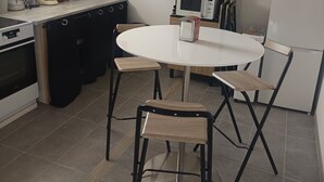 A compact kitchen with a round dining table, black stools, a microwave, a coffee maker, and a refrigerator. - Apartment with exterior (Mirebeau)