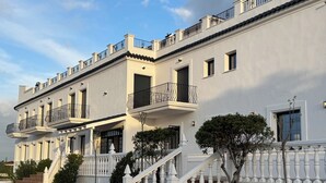 Un immeuble à plusieurs étages doté de balcons, d’un escalier et d’une entrée fermée par un portail.