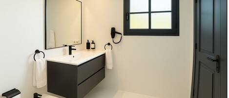 Un baño moderno con un mueble de tocador oscuro, un lavamanos blanco, un bidé y un espejo grande.