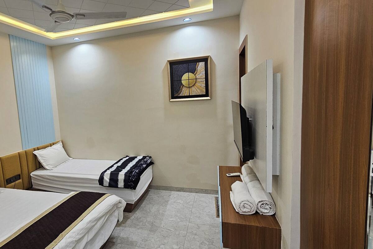 A hotel room with two beds, a TV, a ceiling fan, a painting, and a wooden side table with towels.