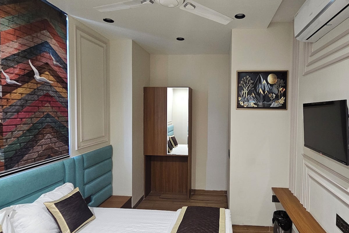 A hotel room with a bed, a TV, a mirror, and a colorful wall mural.