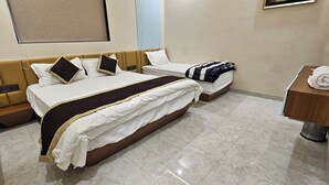 A hotel room with a large bed, a smaller bed, a wooden nightstand, a bathroom with a sink and mirror, and a wall-mounted TV. - Hotel Nexus Inn (Ahmedabad)