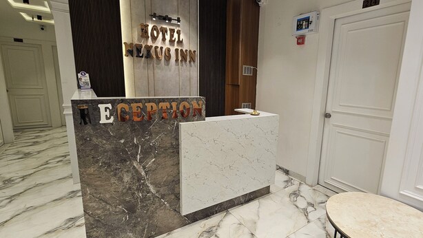 A hotel reception desk with a marble counter, a reception sign, and a door to the right. - Hotel Nexus Inn (Ahmedabad)