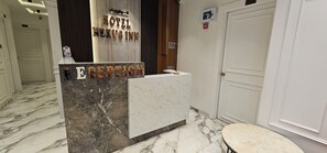 Un mostrador de recepción de hotel con encimera de mármol, un cartel de recepción y una puerta a la derecha.