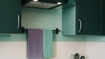 Una cocina moderna con una placa de inducción negra, una olla morada y un hervidor celeste.