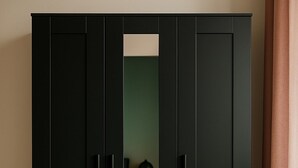 A black wardrobe with a mirror and a small table with a lamp.