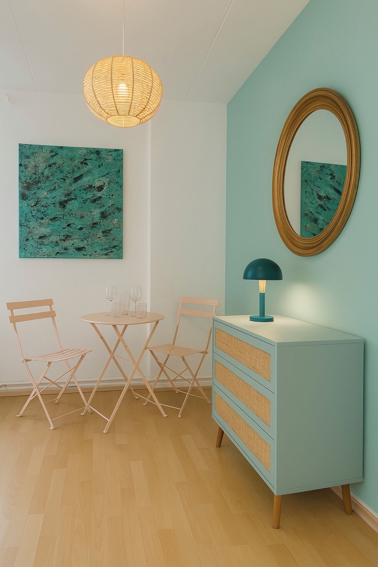 A dining area with a round table, two chairs, a wall-mounted mirror, and a hanging light fixture.