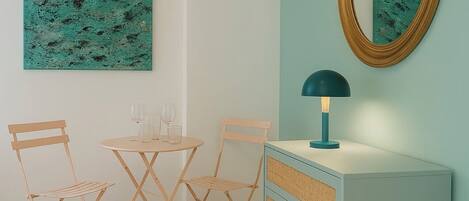 A dining area with a round table, two chairs, a wall-mounted mirror, and a hanging light fixture.
