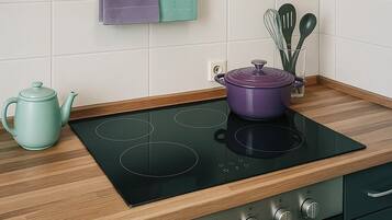 Una cocina moderna con una placa de inducción negra, un hervidor celeste y una olla morada.