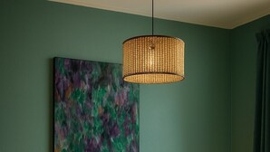 A bedroom with a dark blue bed, two bedside tables with lamps, a woven pendant light, and a large abstract painting on the wall.
