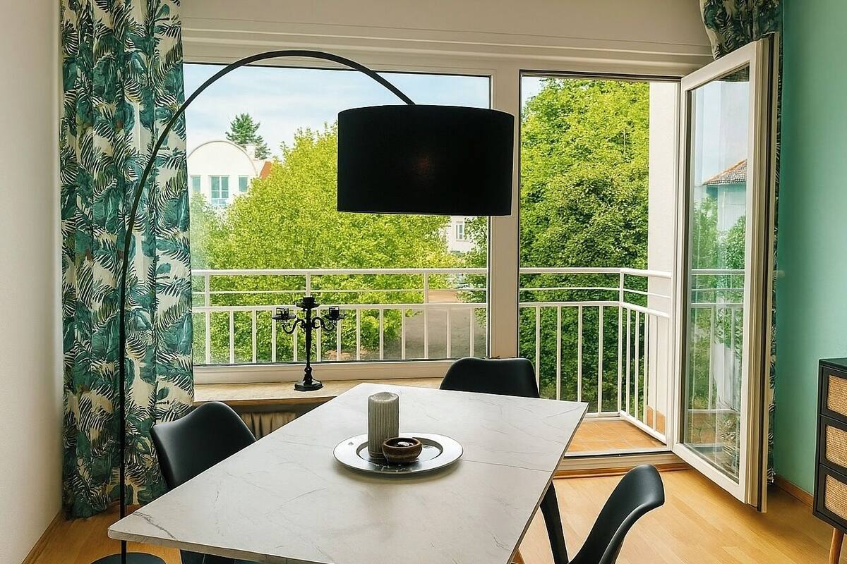 Een eetgedeelte met een tafel, stoelen, een kandelaar en uitzicht op een balkon met beplanting.