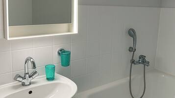 A bathroom with a white sink, a mirror, a shower, and a glass of water.