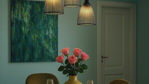 A dining room with a round table set for four, featuring a marble top, gold and black plates, and a yellow vase with pink roses.