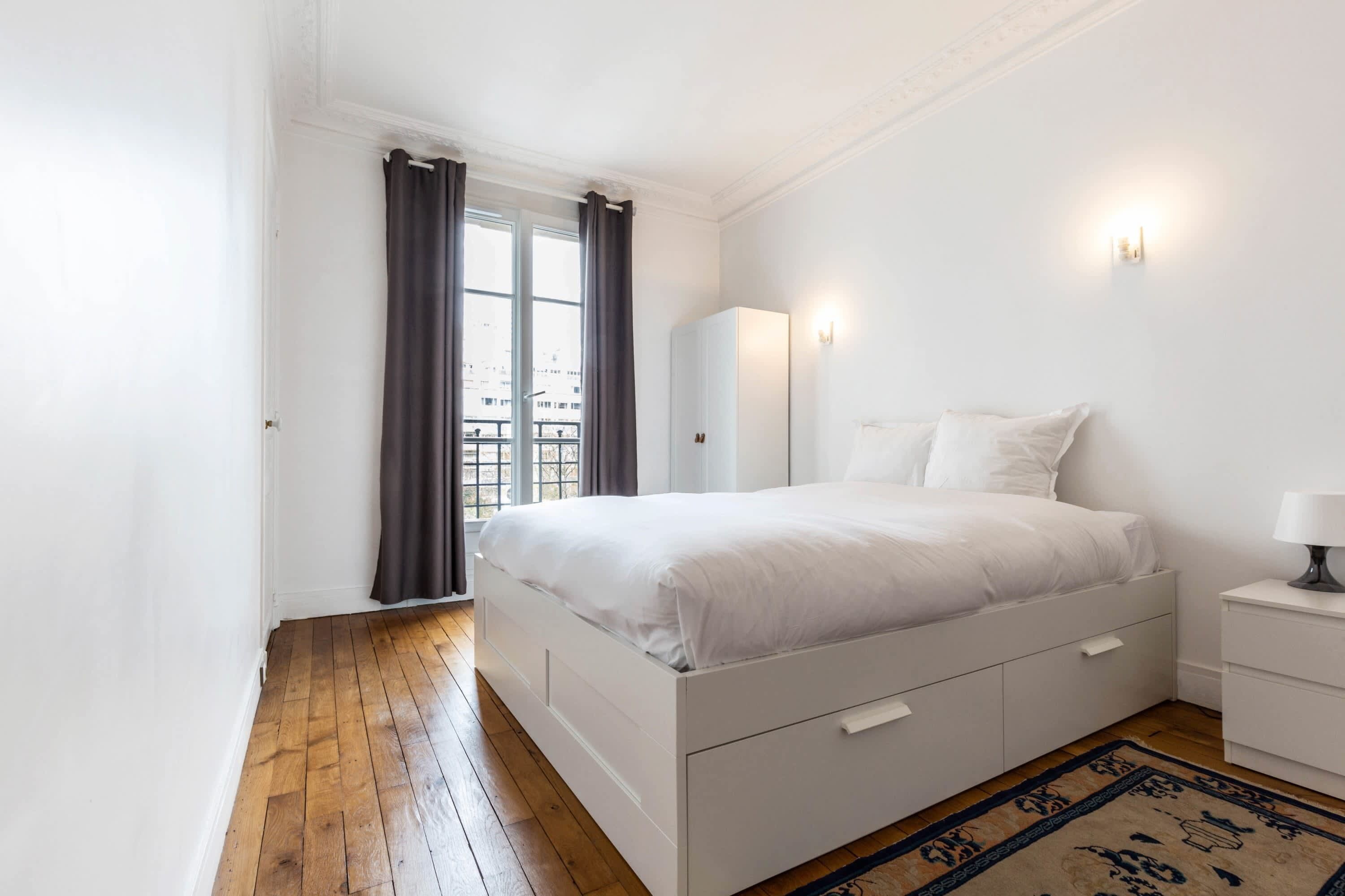 Une chambre à coucher avec un lit, une table de chevet, une armoire et une vue sur la ville par la fenêtre.