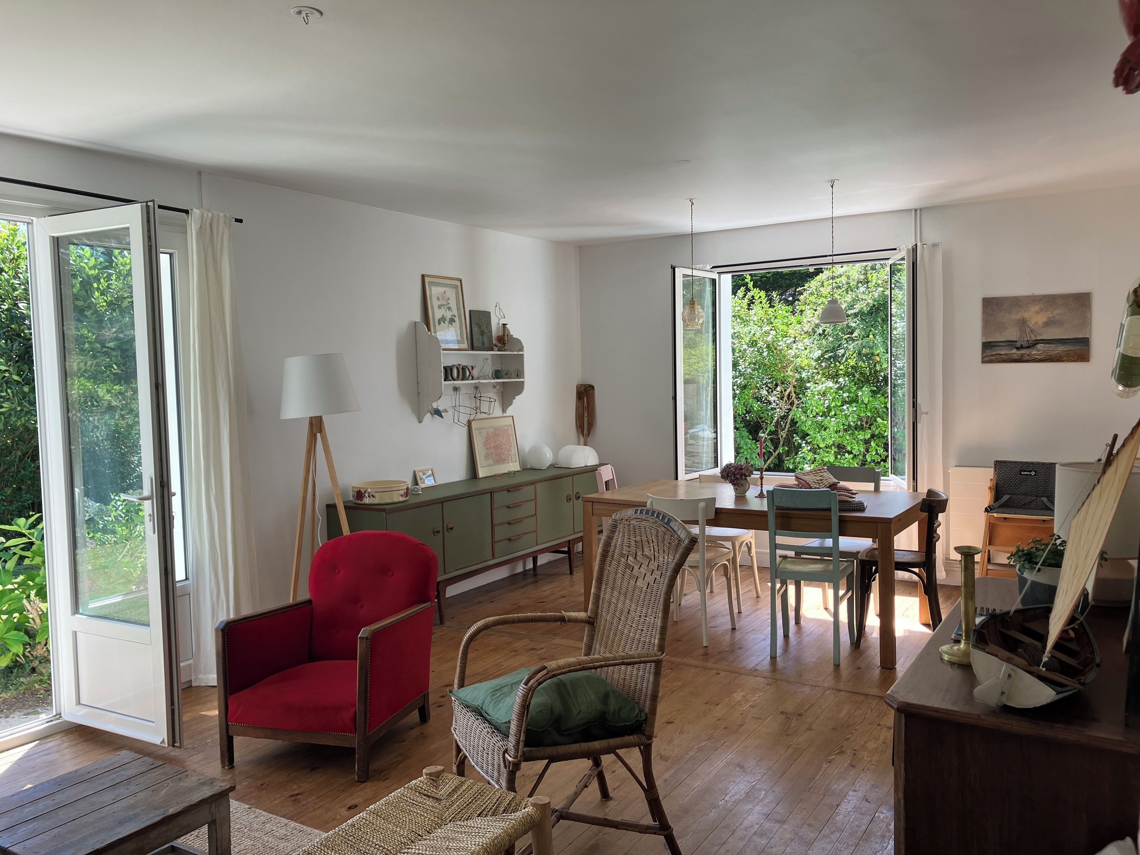Una habitación amplia con suelo de madera, una mesa de comedor, sillas, un sillón rojo, un sillón verde y un aparador con adornos.