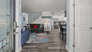 A modern living room with a gray sofa, a patterned rug, and a staircase leading to a kitchen area. - Bombastic Bungalow Beach Home, just a 9 minute walk from the beach! (Panama City Beach)