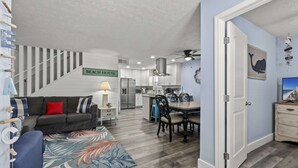 A modern kitchen with white cabinets, a stainless steel refrigerator, and a dining area with a wooden table and chairs. - Bombastic Bungalow Beach Home, just a 9 minute walk from the beach! (Panama City Beach)