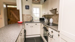 Une cuisine avec des meubles blancs, un plan de travail en granit, un four à micro-ondes, une bouilloire et une horloge murale.