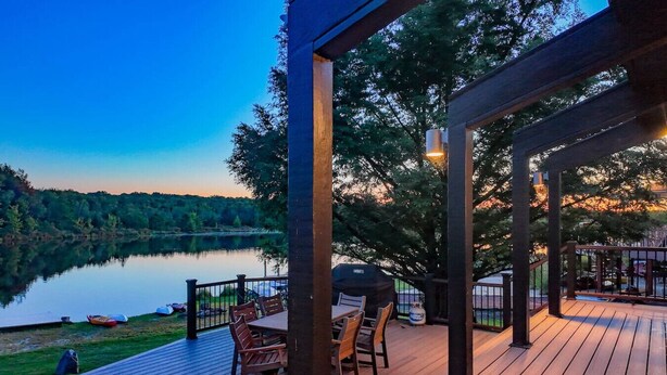 A wooden deck with outdoor furniture, a grill, and a view of a lake at dusk. - Lake Front - Spacious - Outdoor (Albrightsville)
