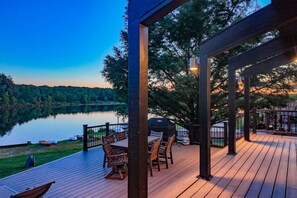 A wooden deck with outdoor furniture, a grill, and a view of a lake at dusk. - Lake Front - Spacious - Outdoor (Albrightsville)