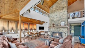 A spacious living room with a stone fireplace, leather sofas, and a dining area with wooden chairs. - Lake Front - Spacious - Outdoor (Albrightsville)