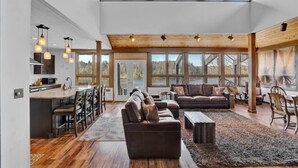 A spacious living area with a high ceiling, large windows, and a kitchen area with bar seating. - Lake Front - Spacious - Outdoor (Albrightsville)