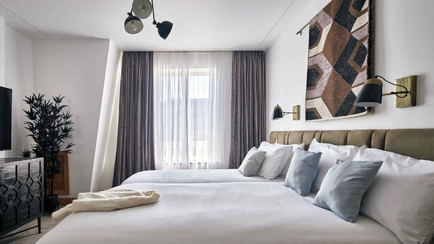 Una habitació d'hotel moderna amb un llit gran, una televisió, una planta i una obra d'art mural amb formes geomètriques.
