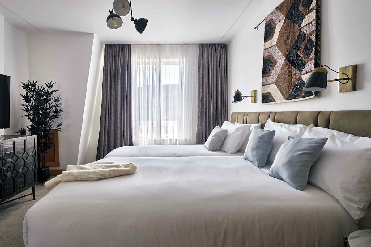 A modern hotel room with a large bed, a television, a plant, and a geometric wall art piece.