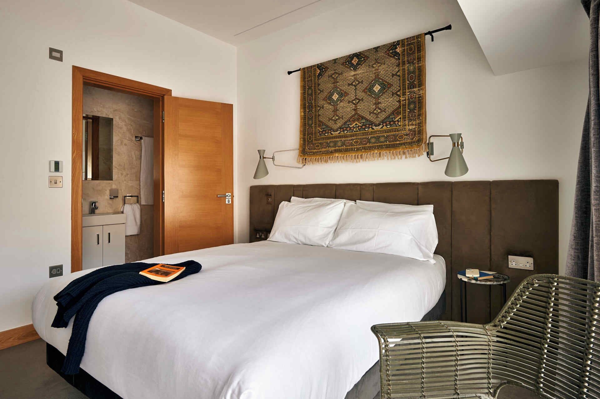 Ein Hotelzimmer mit einem großen Bett, einer Holztür, einem Badezimmer mit Spiegel, einer Wandleuchte und einem Wandteppich mit Muster.