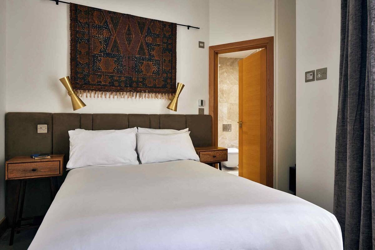 A neatly made bed with white linens, a brown upholstered headboard, and two bedside tables with lamps.