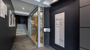 Rebedor modern d'hotel amb una porta de vidre que dona a una escala, una desfeta digital per a l'eixida i pòsters informatius a les parets.
