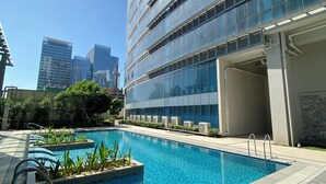 Ein modernes Gebäude mit Glasfassade, einem Schwimmbecken mit Holzterrasse und blauem Himmel.