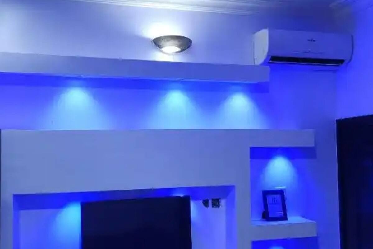 A room with a flat-screen TV on a stand, a ceiling light fixture, and an air conditioning unit mounted on the wall.