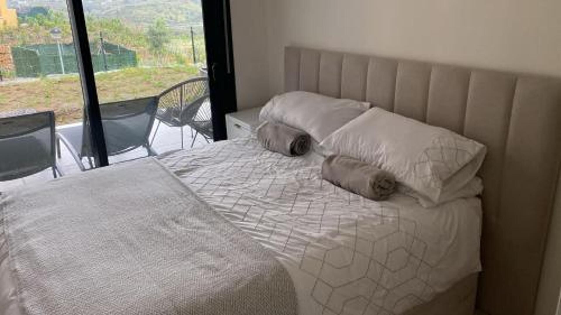 Ein Schlafzimmer mit Bett, Stuhl und Blick ins Freie.