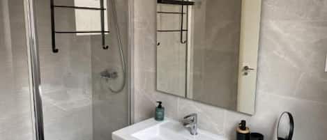 Une salle de bain moderne avec une douche à parois de verre, un grand miroir, un lavabo blanc et un porte-serviettes.