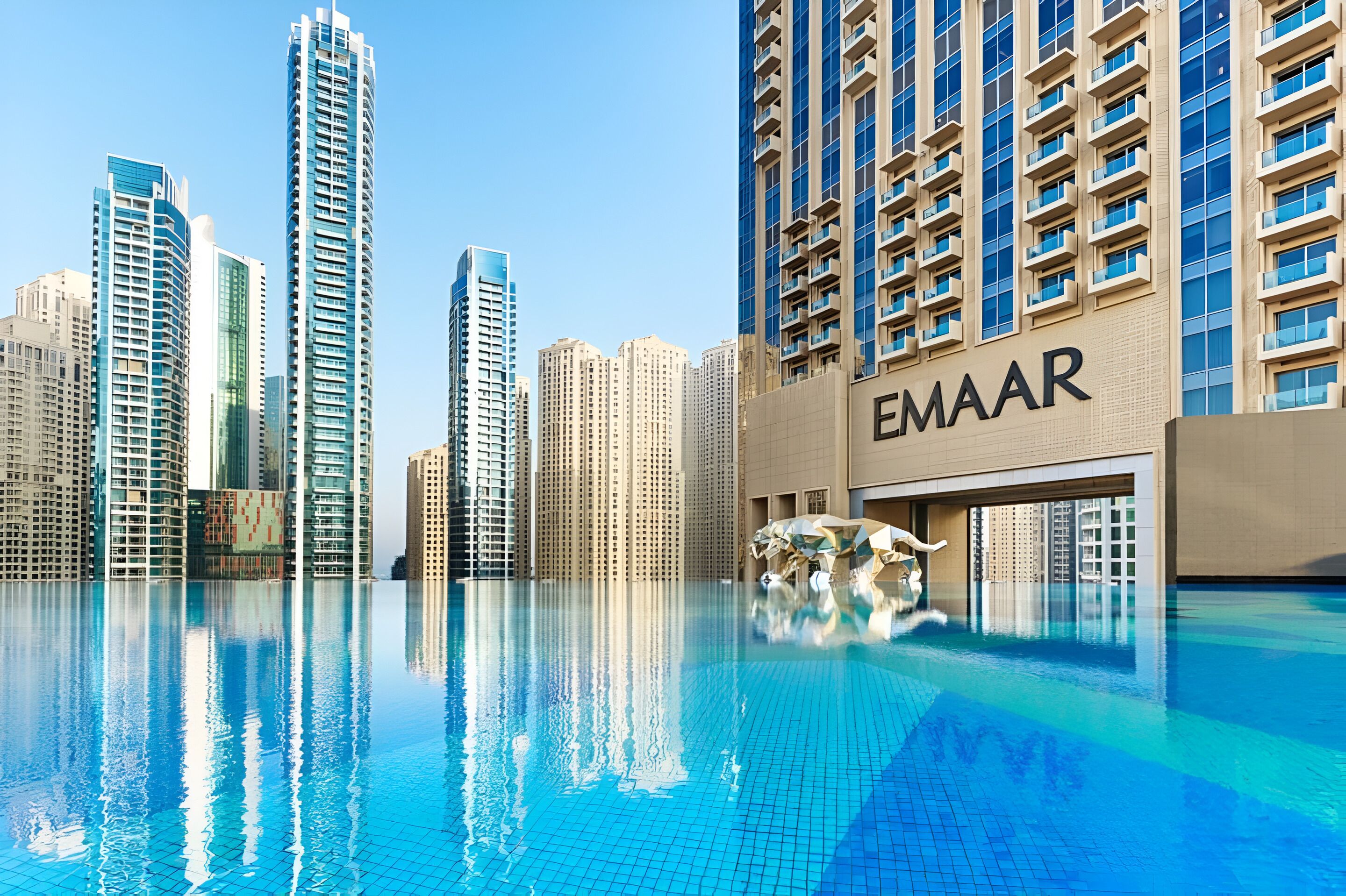 A modern hotel with a pool, high-rise buildings in the background, and the name 'EMAAR' on the facade.