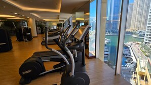 A gym with treadmills and exercise equipment, large windows with a view of a marina and high-rise buildings.