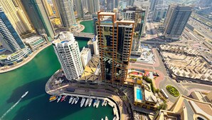 A high-rise building with a unique geometric design, surrounded by other modern skyscrapers and a marina with boats.