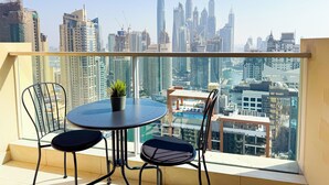 A balcony with a table and chairs, a potted plant, and a cityscape view.