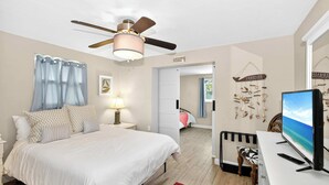 A bedroom with a bed, a desk, a television, a ceiling fan, and a door leading to another room. - Tranquil Pool Home Near Siesta Key (Sarasota)