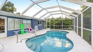 A covered outdoor swimming pool with a glass enclosure, a blue exterior wall, and a green inflatable ring. - Tranquil Pool Home Near Siesta Key (Sarasota)