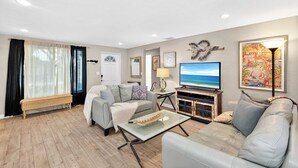 A living room with a grey sofa, a coffee table, a TV, and artwork on the walls. - Tranquil Pool Home Near Siesta Key (Sarasota)