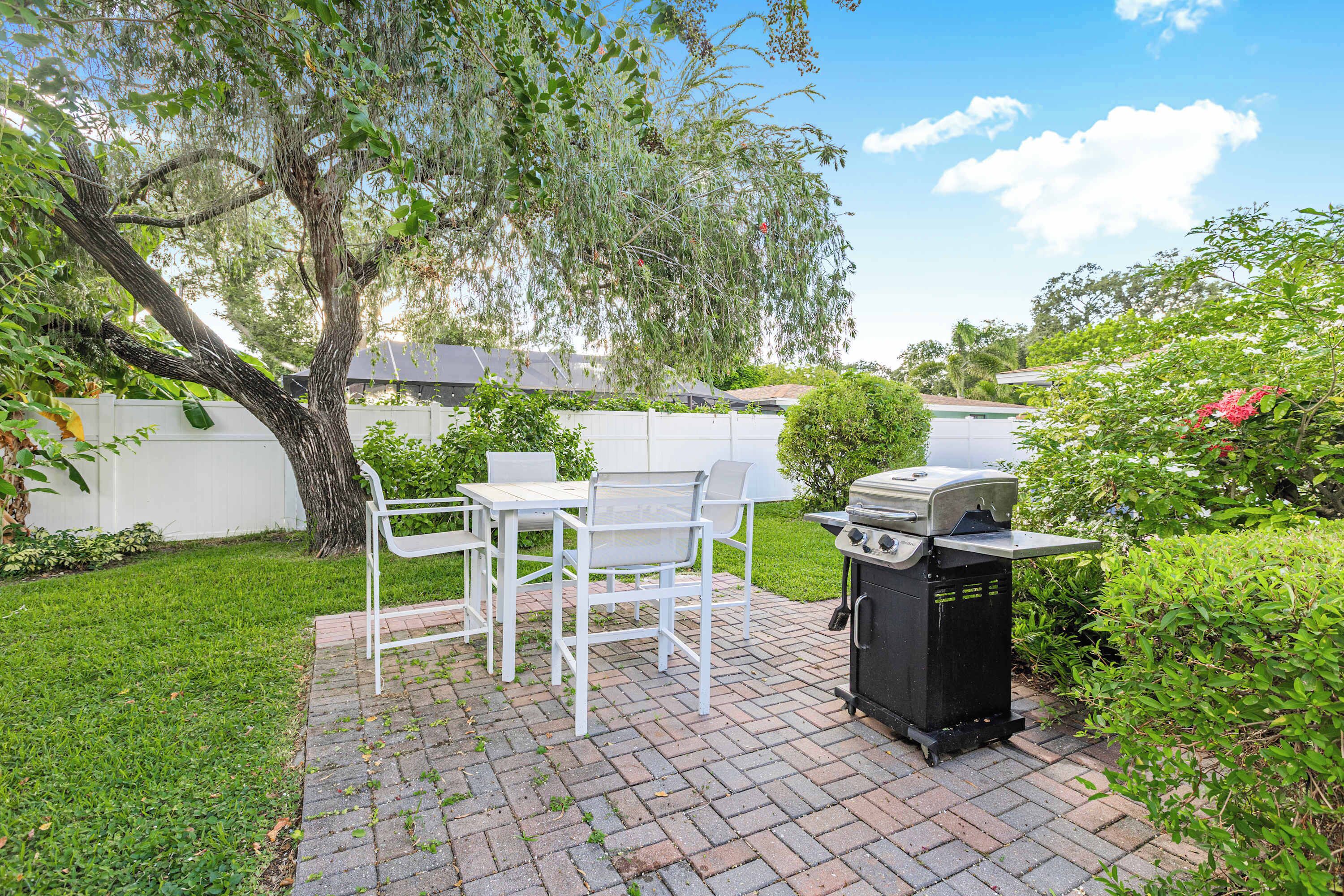 A patio with a grill, white chairs, and a tree.