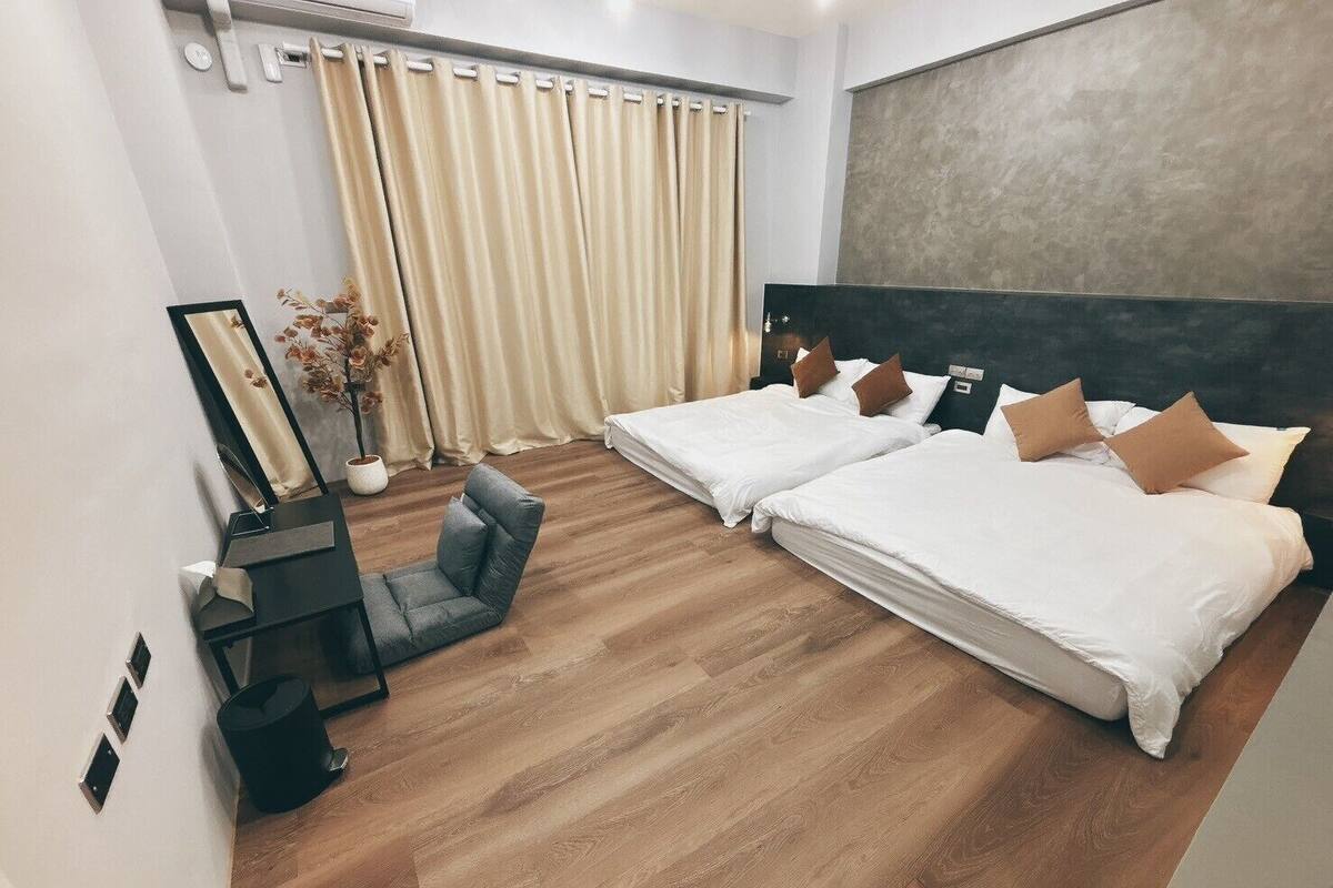 A hotel room with two beds, a desk, a chair, and a large window with curtains.