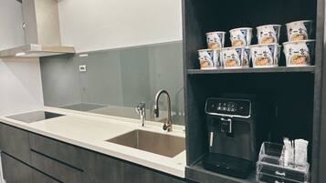 A modern kitchen with a built-in sink, a coffee machine, and shelves with packaged goods.