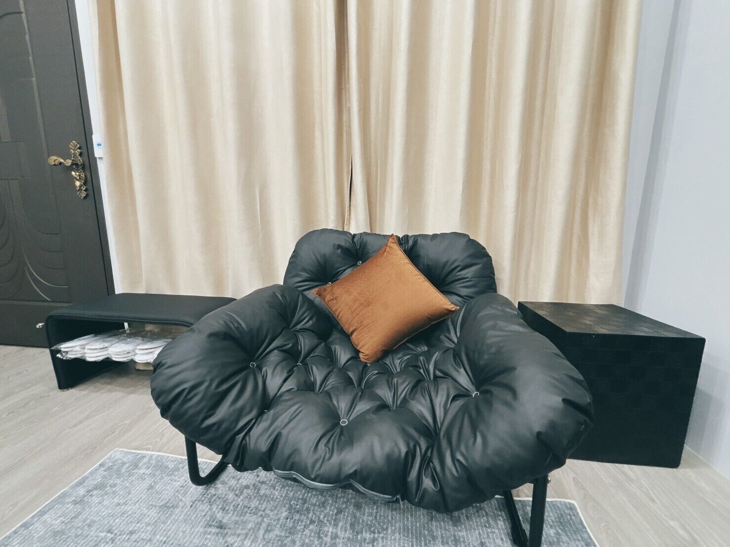 A black leather armchair with a brown cushion in a room with a wooden floor, a grey rug, and a dark wooden cabinet.