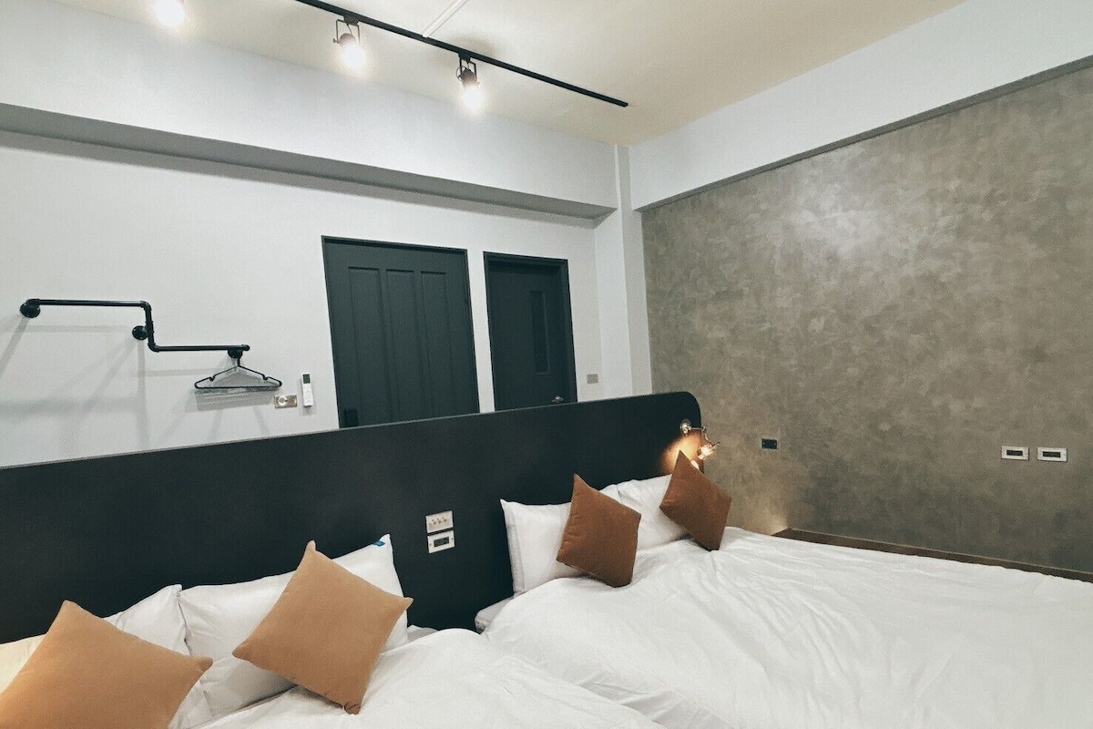 A modern bedroom with a large bed, a black headboard, and a grey textured wall.